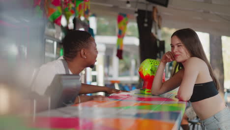 bartender flirts with lady at counter in summer bar. african american man wipes countertop sweetly talking with young woman in bar. customer service