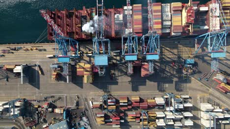 aerial top down truck right of cranes loading containers on a cargo ship docked in valparaiso sea port, chile