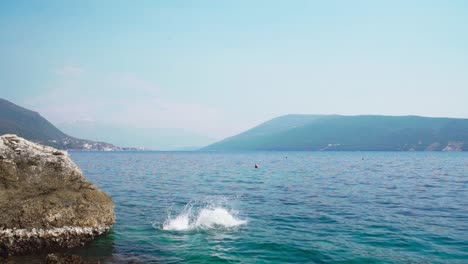 Adult-woman-jumping-off-from-a-rock-into-the-sea-water-on-a-clear-day