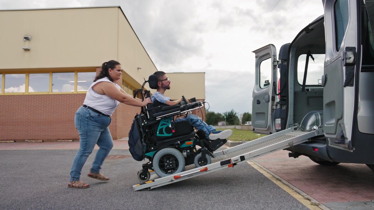 Assistente pessoal acompanhando um usuário de cadeira de rodas motorizada para um veículo adaptado usando um.