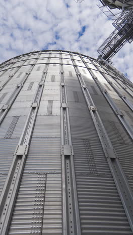 large metal grain elevator outdoors. modern silver granary on sky background. huge aluminum container for storing crop. view from below. vertical video