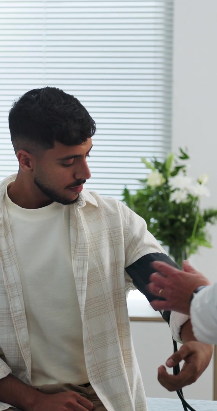 Læge måler blodtryk på ung mandlig patient