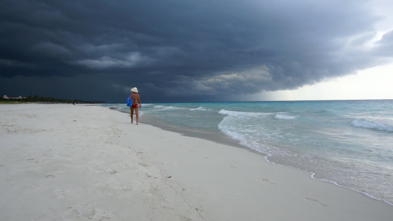 woman walks on a beautiful tropical beach of fine sand and in the background the sky is all black for the arrival of a tropical storm.slow motion.