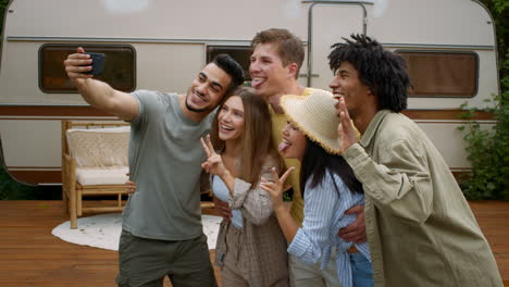 group of friends taking a selfie outdoors near a camper