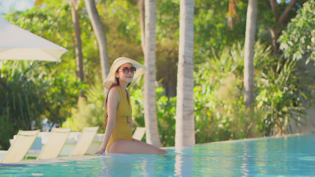 AN attractive young woman in a bathing suit sits on the edge of a resort pool lounging in the shallow water. Copy space