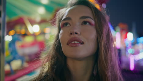 portrait beautiful funfair girl look camera in colourful blinking bokeh lights.