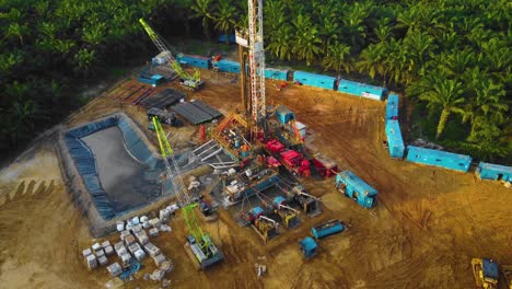imágenes cinematográficas de drones de 4k de la estructura del equipo de la plataforma de perforación en tierra para la exploración y explotación de petróleo en medio de la jungla rodeada de palmeras durante la puesta de sol y el alto precio del petróleo
