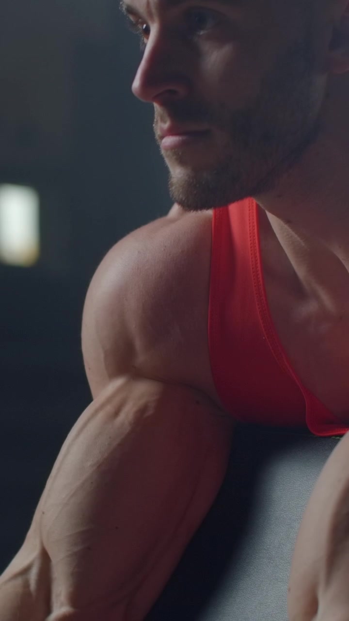 Uomo muscoloso che esegue curl per bicipiti con bilanciere EZ in palestra