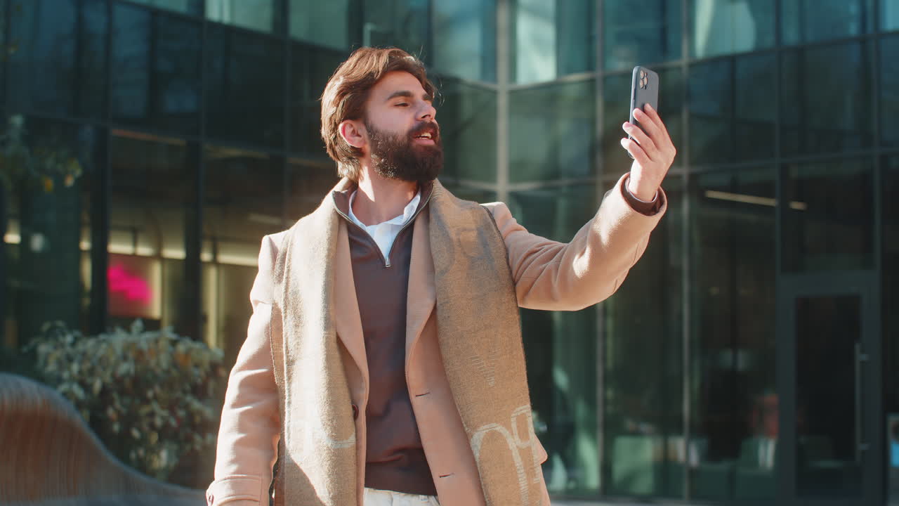 Indian man blogger taking selfie on smartphone video call online with subscribers on city street