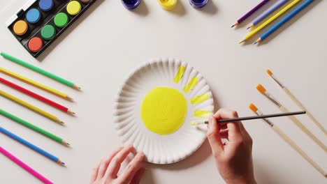 video of hands painting design on paper plate, with art materials arranged on white background