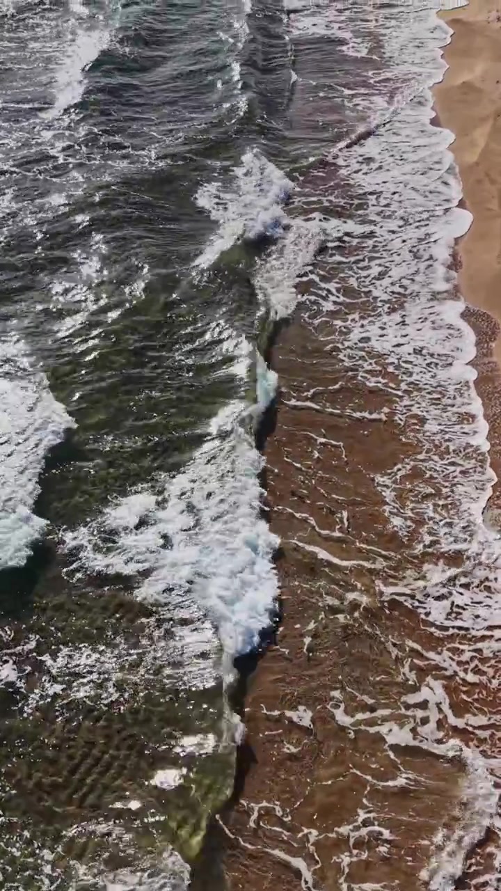 Onde che si infrangono su una spiaggia sabbiosa al tramonto da una vista aerea