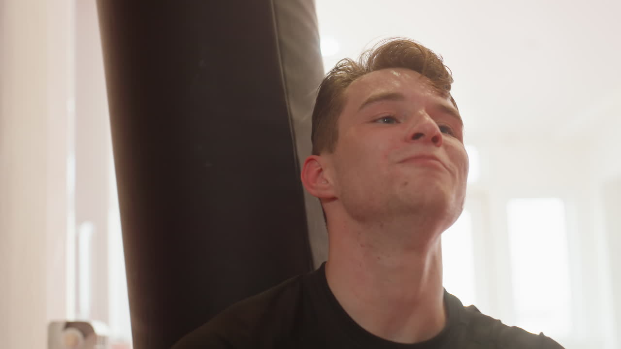 Boxer with sweaty face smiling after intense training session in gym, showing relief, satisfaction, determination, and positive energy while recovering from physical workout with strength