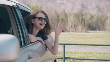 dama con gafas de sol se inclina hacia fuera del coche agitando la mano en un buen día