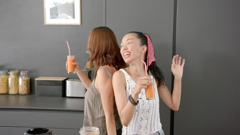 two young biracial female friends enjoy drinks and a dance in a kitchen