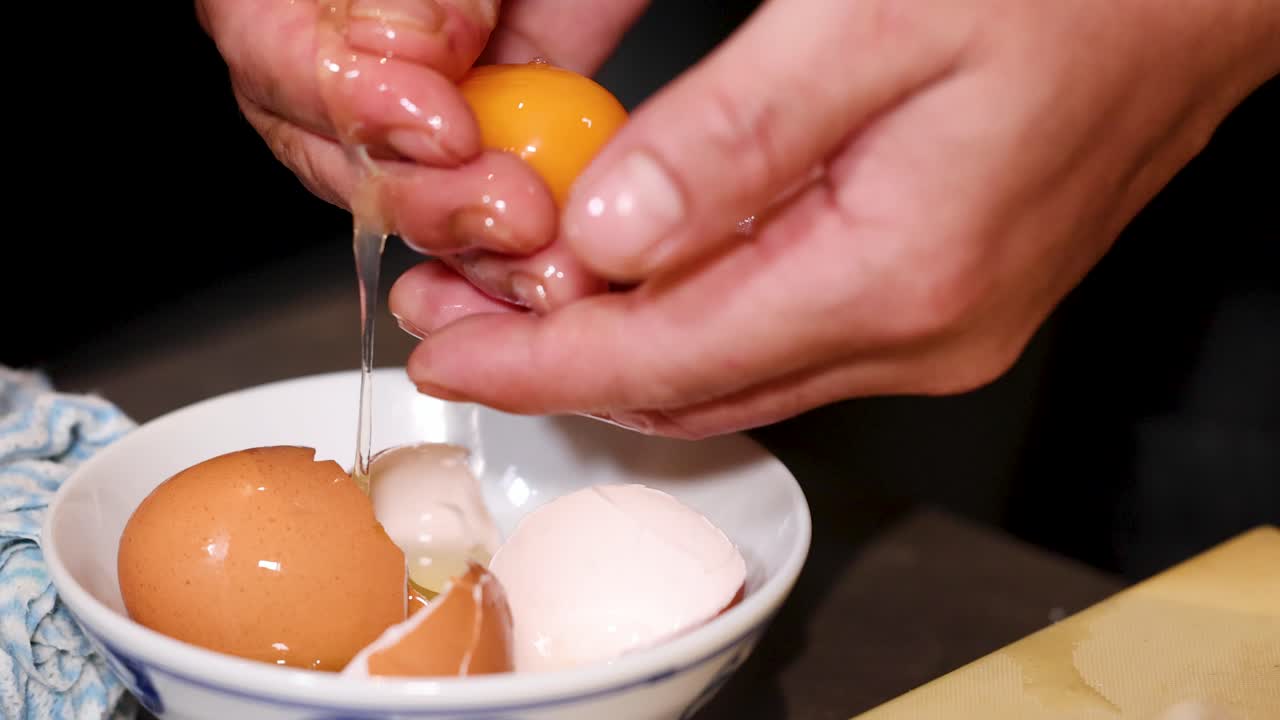 Close-up shot of a chef's hands skillfully separating a raw egg yolk over a bowl