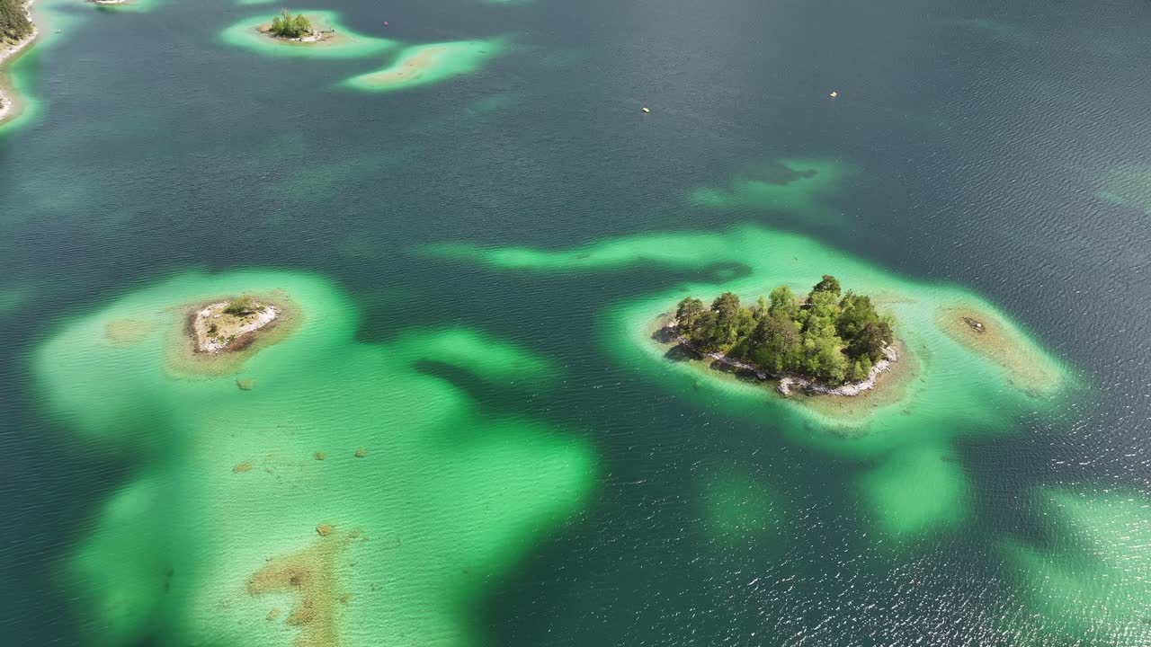 Eibsee's emerald green waters highlighting small, forested islands and sandy shallows in Grainau, Germany - aerial