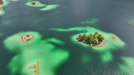 Las-Aguas-Verde-Esmeralda-Del-Eibsee-Resaltan-Pequeñas-Islas-Boscosas-Y-Arenales-Poco-Profundos-En-Grainau,-Alemania---Vista-Aérea