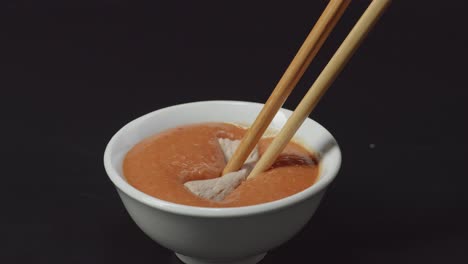 close up of pork dipping to shabu shabu dip sauce by chopsticks on the black background