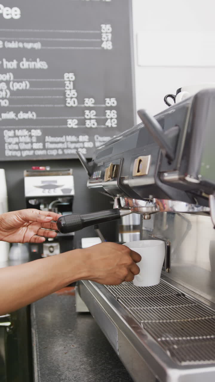Vertical video of biracial female barista preparing coffee in coffee machine in cafe