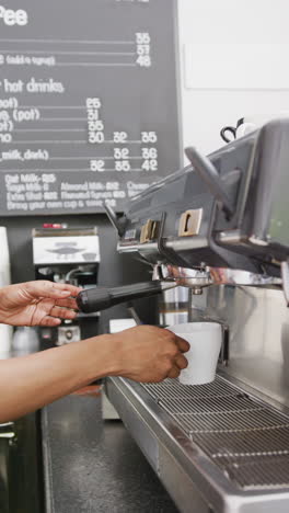 vertical video of biracial female barista preparing coffee in coffee machine in cafe
