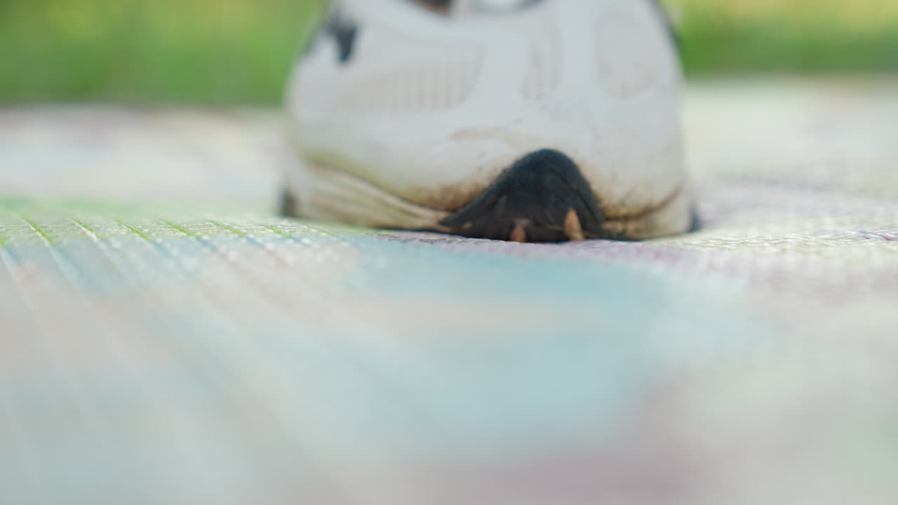 Låg vinkelvy av sneaker på yta. Skodon med nött tå vidrör texturerad markyta. Perspektiv från marknivå som avslöjar sneaker i rörelse med synliga mönsterdetaljer.