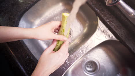 Manos-De-Mujer-Lavando-Un-Calabacín-Verde-En-La-Cocina-En-Cámara-Lenta,-Vista-Superior