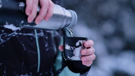 thermos pours tea into mug in the middle of cold winter landscape