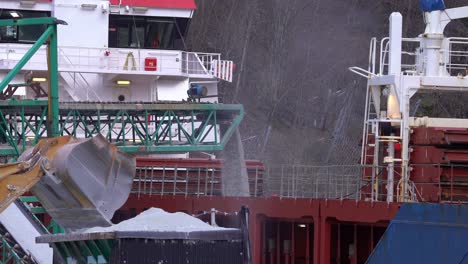 dumper emptying his bucket of anorthosite in conveyor belt container before pulling out of frame to the left - dust flying around - port of gudvangen norway