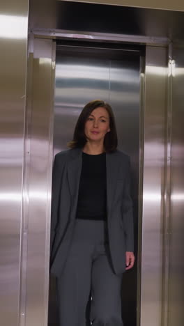 businesswoman walking out of elevator, dressed in gray suit, confident expression, modern office building, professional attire, career success, corporate setting, workday