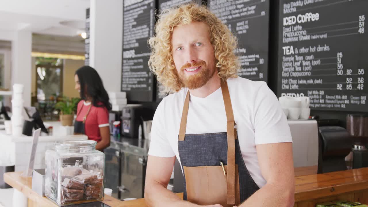 Portrait of happy caucasian male barista using tablet, smiling behind the counter in cafe