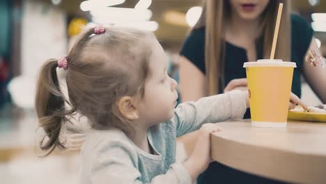 mom feeds a little daughter with a fork they sit in a cafe