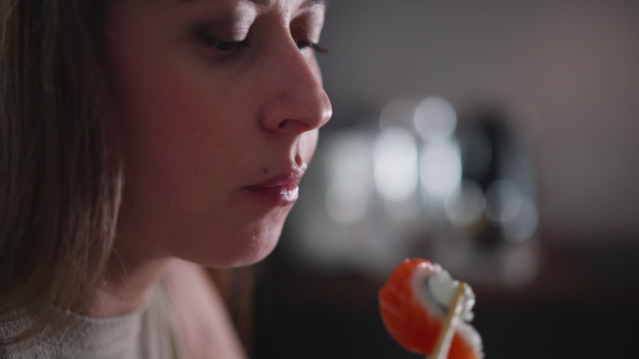 Close up of white lady carefully eating sushi with chopstick, thoughtful expression on her face, soft light highlighting skin texture, background features beautiful bokeh effect