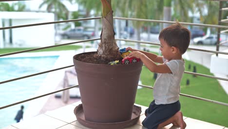 Little-latin-baby-boy-playing-on-the-dirt-in-a-plantpot-at-his-home-balcony-watching-the-people-in-the-common-areas