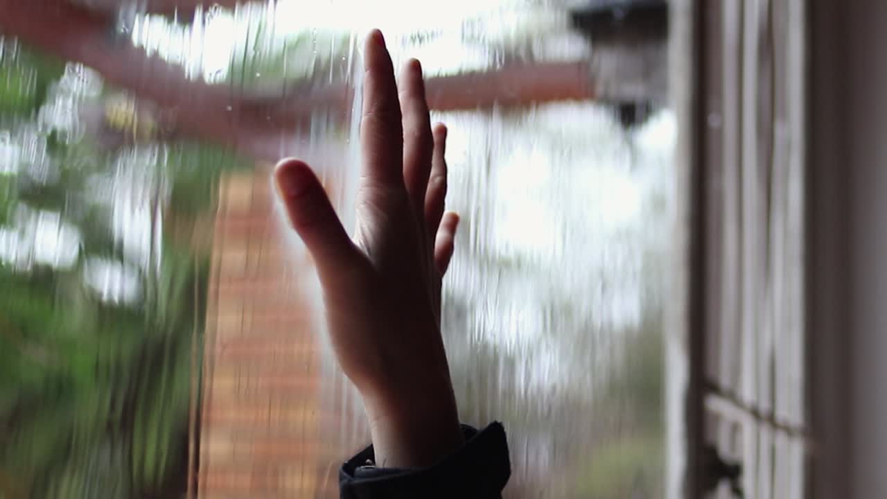 Child removes hand from rainy window pane leaving wet imprint on glass