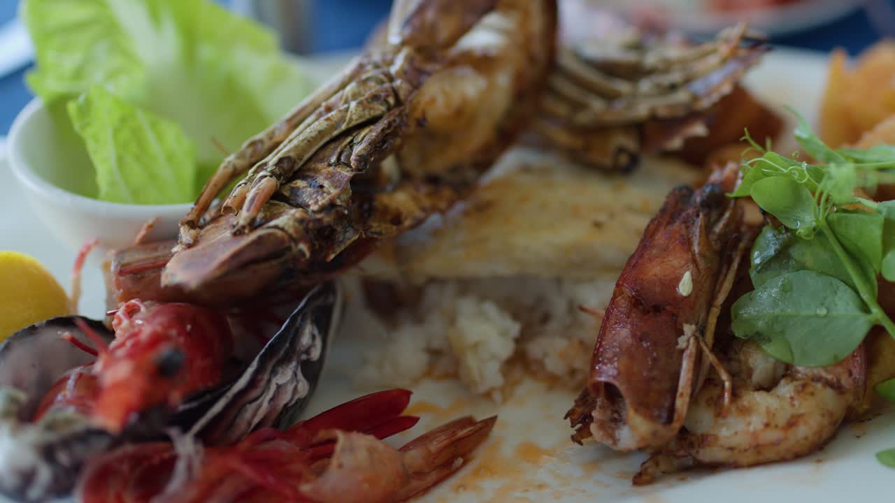 Camera slowly pans across fresh grilled prawns, shellfish, greens, and lemon under natural lighting