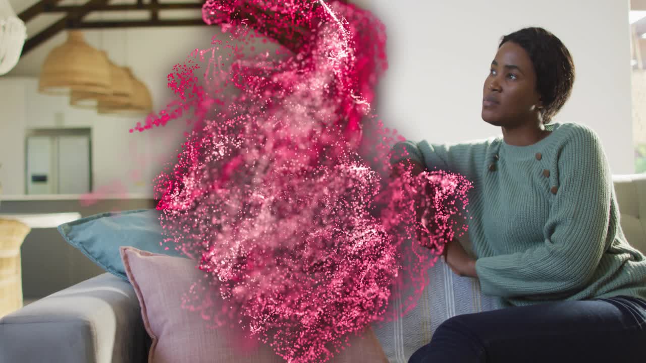 Woman seated right couch watching pink particles emerging left seat, adjusting elbow for tech demo