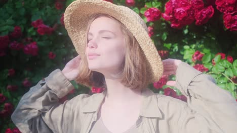 elegant beautiful blonde young woman in a straw hat on the background of a bush of blooming roses