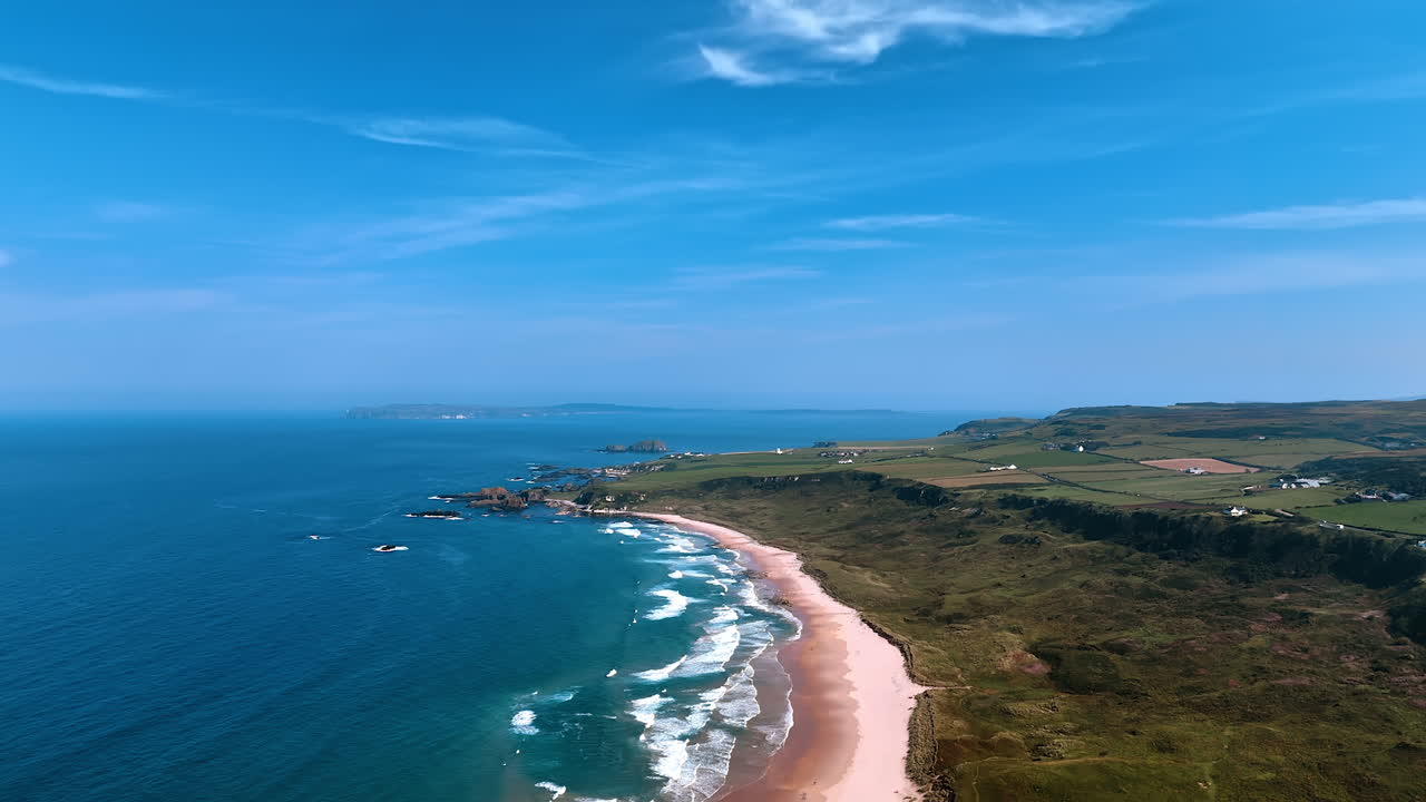 Capturing scenery of the Atlantic ocean at the coast of Ireland. Sandy beach and green valley with some houses and farm fields on from drone footage.