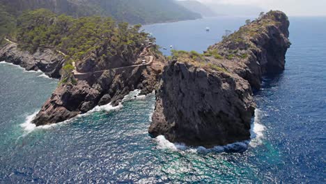 Kreisen-Sie-Um-Eine-Raue-Klippenbucht-Mit-Bewölkten-Bergen-Und-Yachten-Im-Hintergrund