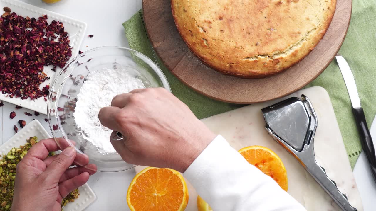 Baking a dessert called Persian Love Cake made with rose petals and pistachios. Cake with white glaze frosting. Mixing icing in a bowl. Beautiful cake for tea time or celebration