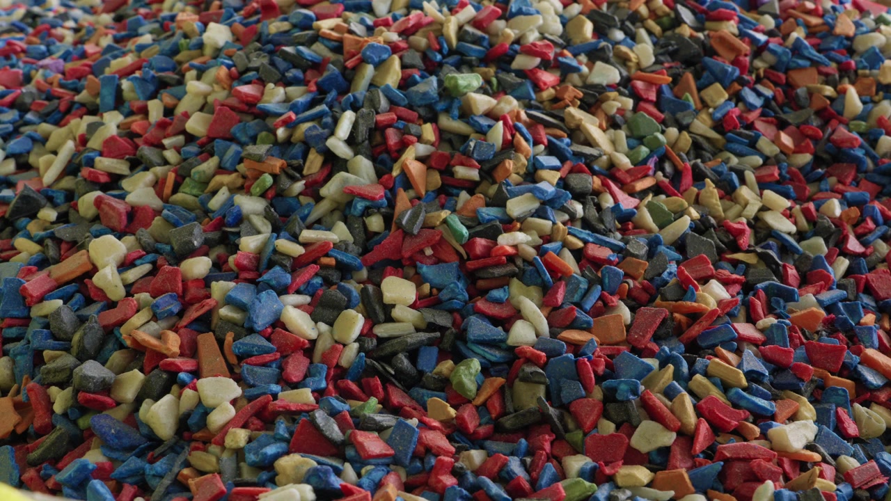 Dense pile of colorful mixed recycled plastic granules in red blue beige green filling entire frame