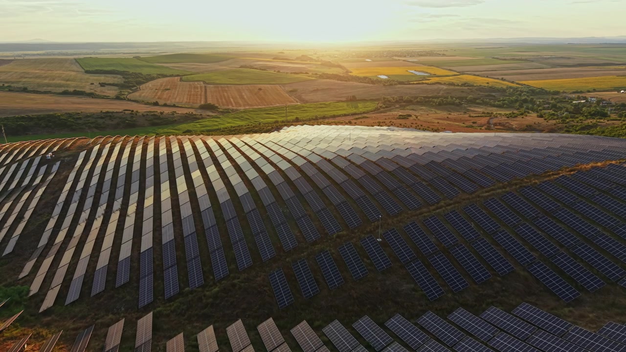 Solnedgang over stor solcellepark med rækker af solpaneler på en åben mark