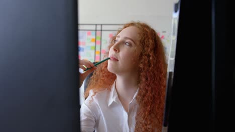 Front view of thoughtful young caucasian businesswoman touching her lip with a pencil at desk 4k