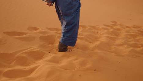 a desert guide in blue robe walks barefoot on golden sahara sands of morocco