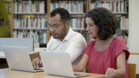 Colegas-Sentados-En-La-Biblioteca-Y-Usando-Computadoras-Portátiles