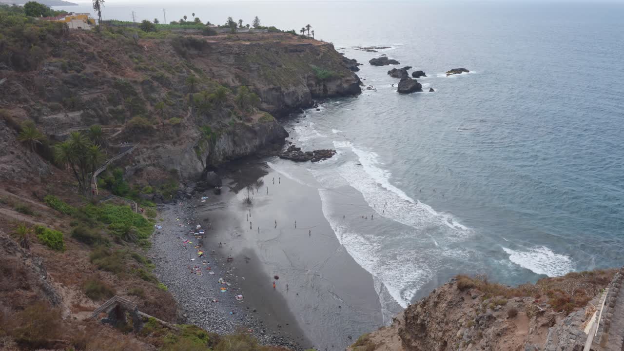 View of people on a volcanic beach and cliffs in Playa de los Roques, Puerto de la Cruz, Tenerife, Spain.