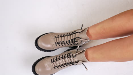 beautiful elegant beige boots with black soles and laces. model sitting and showing the footwear holding shoes by the tongues. top view.