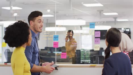 Group-of-diverse-business-people-taking-notes-on-glass-wall-and-talking-in-office,-slow-motion