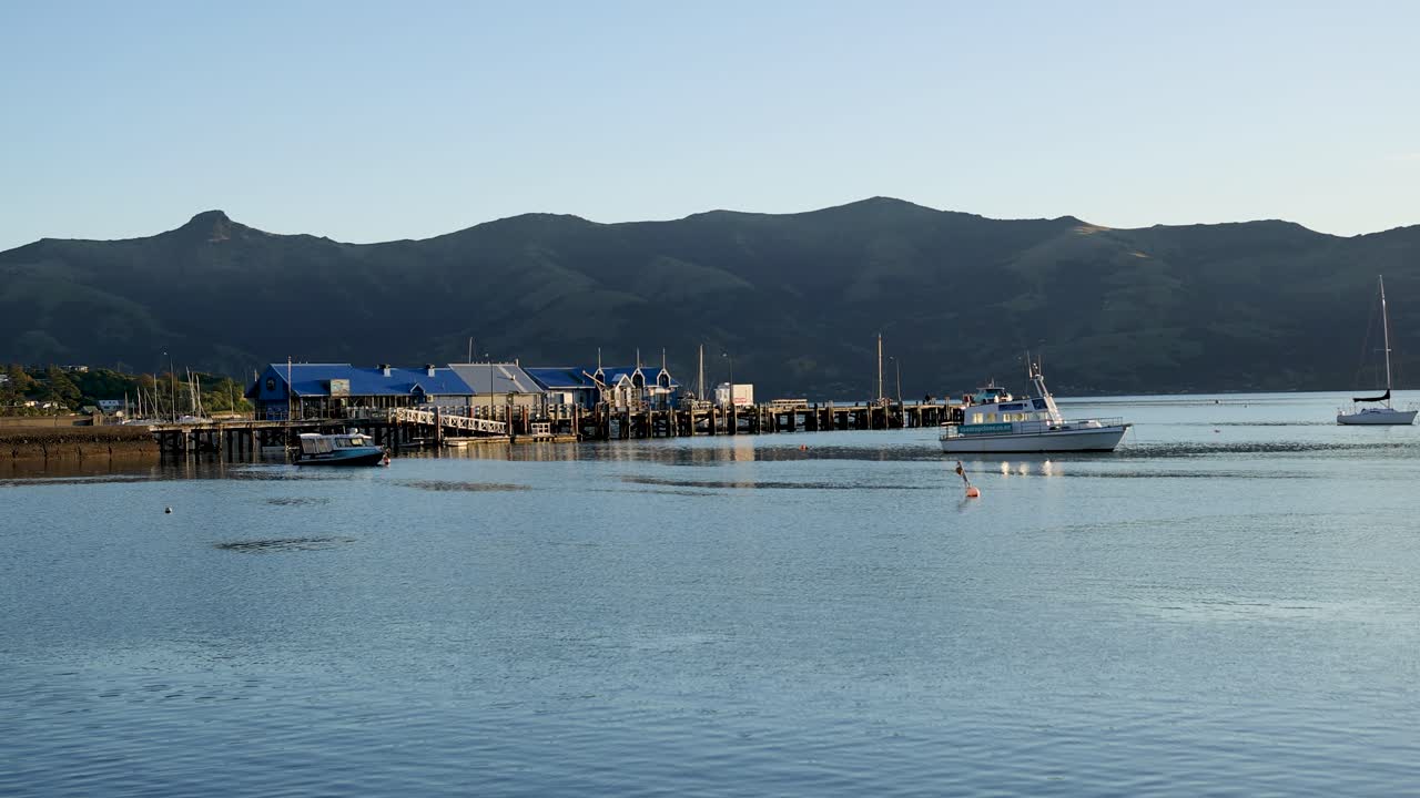 A boat glides through calm waters in Akaroa, New Zealand, under soft evening light, surrounded by tranquil landscapes