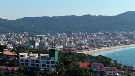 a vibrant city nestled on hills beside water, embraced by lush green mountains on a sunny day. bombas - bombinhas, brazil